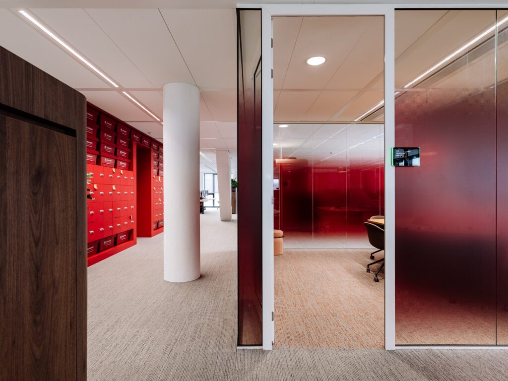 Een moderne kantoorruimte met rode glazen wanden en een muur vol met rode opbergkasten.
