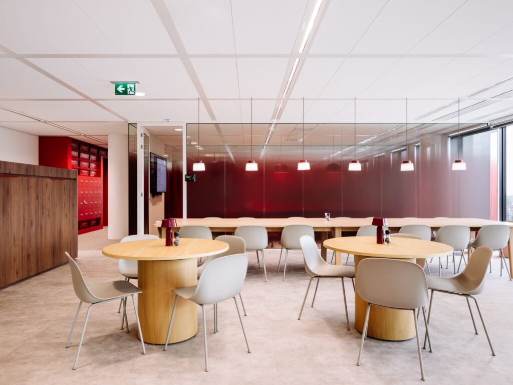 Een moderne kantoorruimte met houten tafels, grijze stoelen en rode accenten.