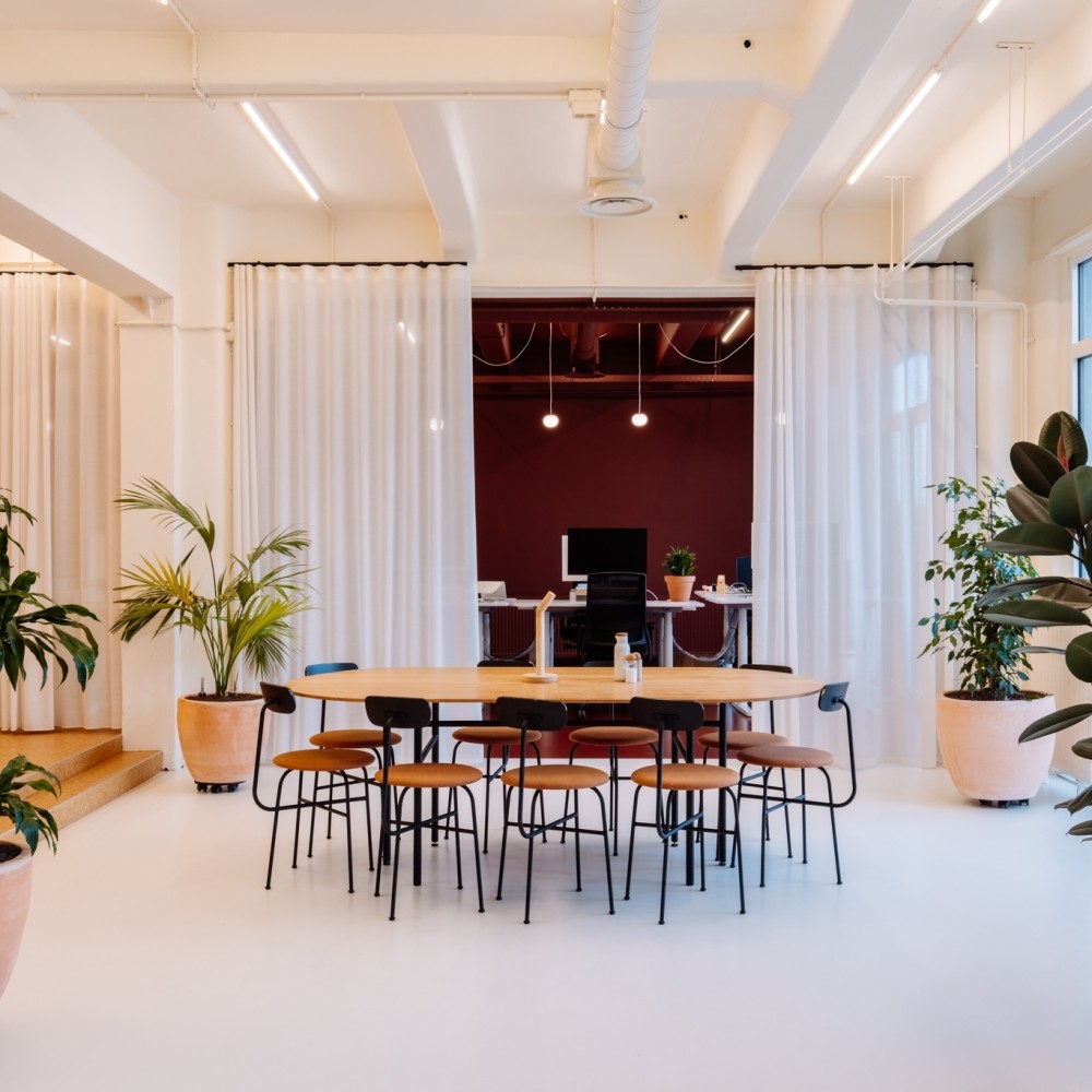 Een moderne vergaderruimte met een grote tafel, omringd door groen, in een kantoorinterieur.