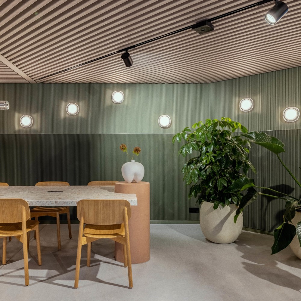 Een moderne vergaderruimte met houten stoelen, een marmeren tafel en groene planten.