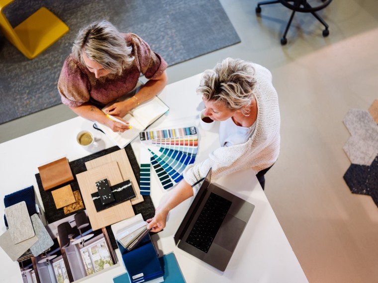 Twee personen bekijken kleurstalen en materiaalmonsters aan een bureau.