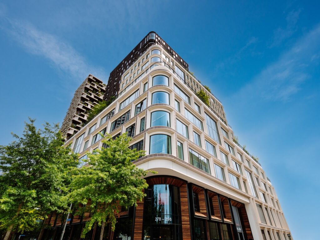 Een modern gebouw met een groene gevel en grote ramen onder een heldere blauwe lucht.