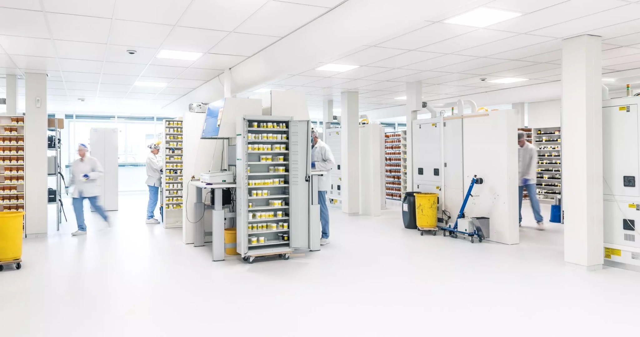 Cleanroom productieruimte met gele en groene kratten en medewerkers in beschermende kleding.