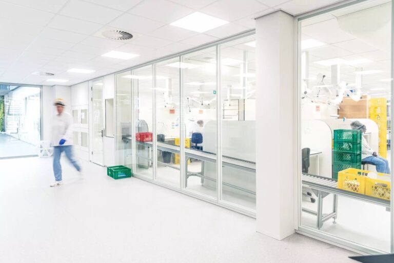 Overzicht van een cleanroom met witte wanden en glazen scheidingswanden, waar mensen in witte kleding werken.