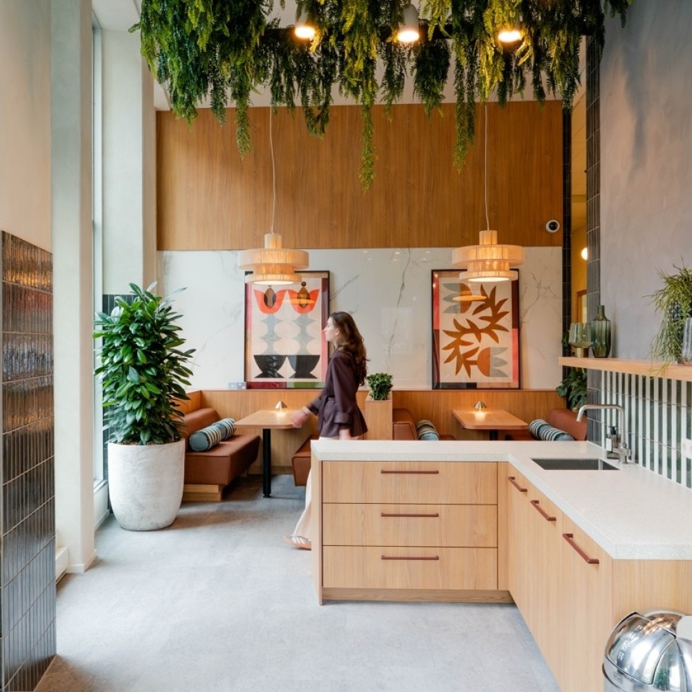 Een moderne coworking keuken en lounge met houten interieur, planten en kunstwerken aan de muur.
