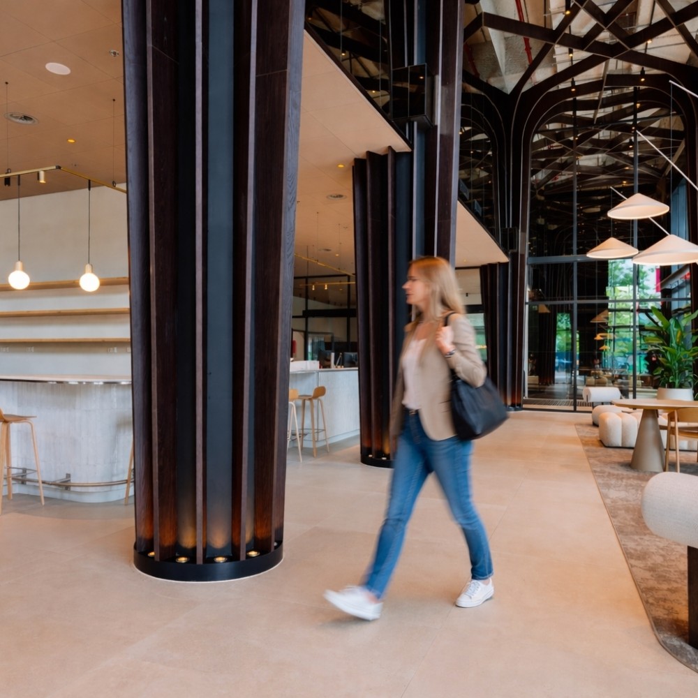 Vrouw loopt door een modern ontworpen coworking lobby met stijlvolle meubels en hoge pilaren.