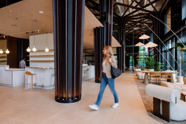 Moderne coworking-ruimte met houten elementen, lounge stoelen, en een persoon die voorbij loopt.