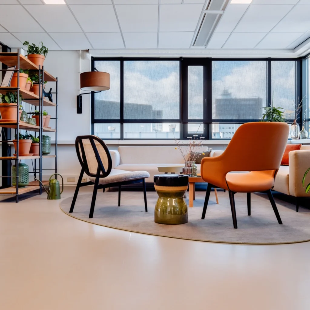 Een moderne loungehoek met diverse stoelen, planten en een groot raam.