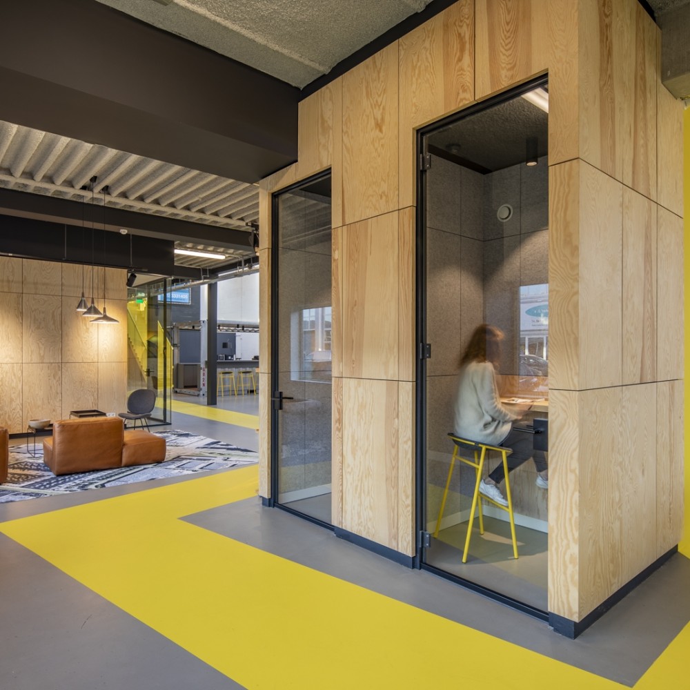 Een moderne kantoorruimte met een houten privé-pod en felgele accenten.