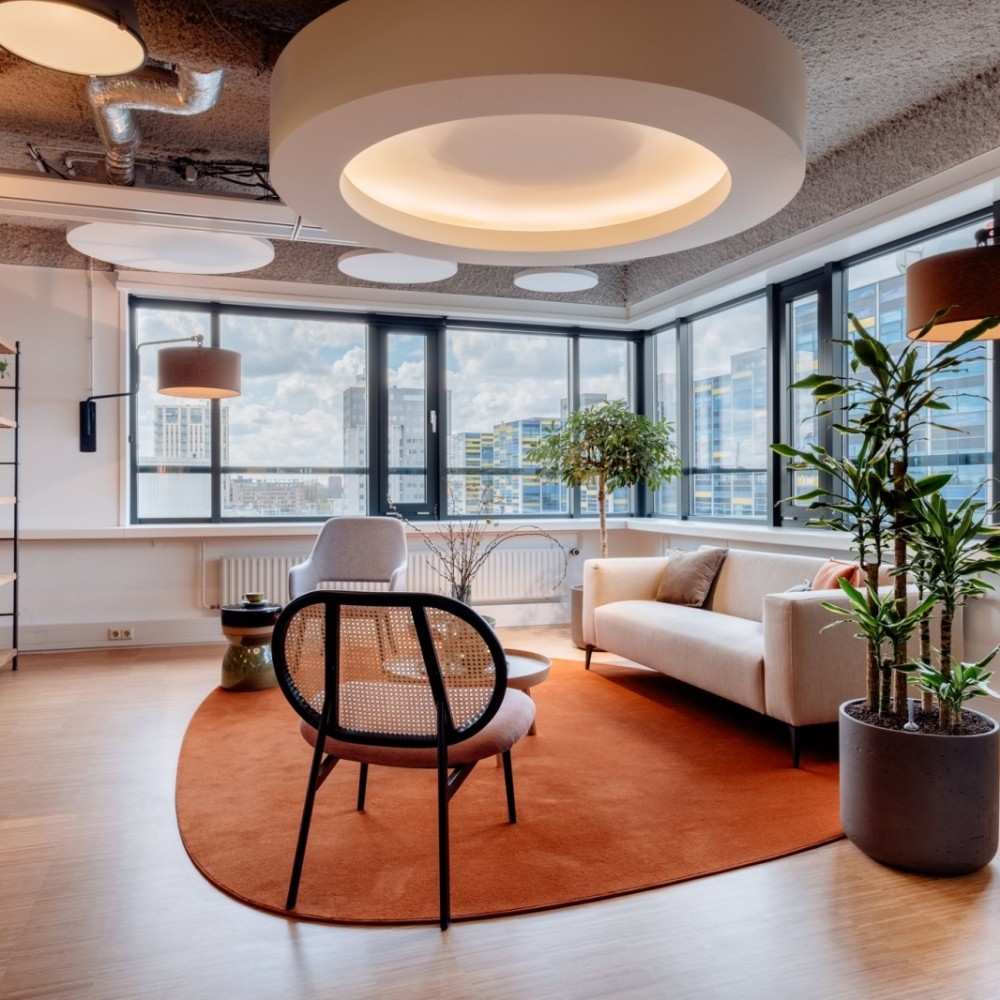 Moderne kantoorruimte met comfortabele zitplaatsen, grote ramen en groene planten.