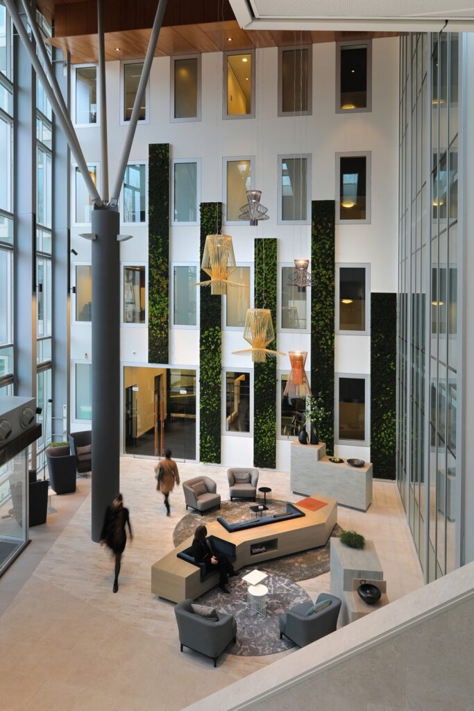 Grote kantooratrium met zitgedeelte, groene wandpanelen en meerdere verdiepingen met ramen.