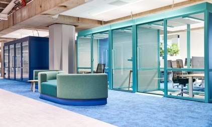 Moderne kantoorruimte met glazen vergaderruimtes en een groene bank.