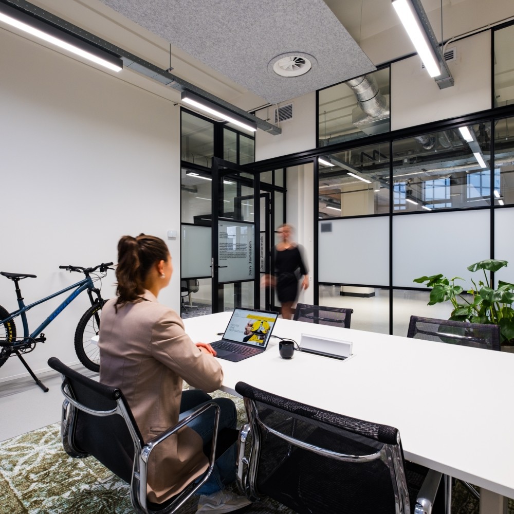 Een persoon werkt op een laptop in een industrieel ingericht kantoor met een fiets aan de muur.