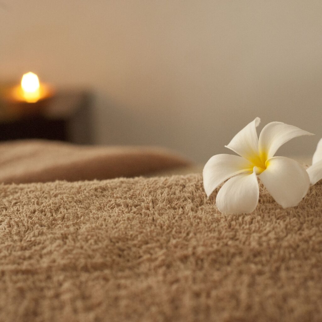 Witte bloem op een zachte handdoek met een brandende kaars op de achtergrond, in een rustgevende spa-achtige setting.