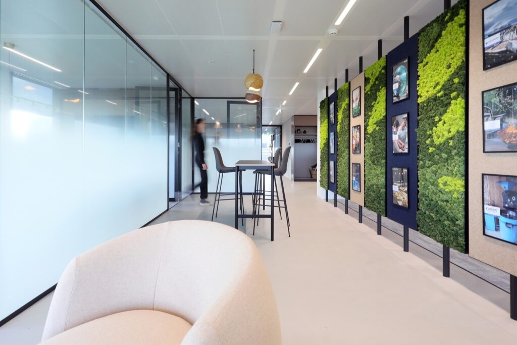 Modern kantoorinterieur met glazen wanden, hoge tafel en groene akoestische panelen met moswand, ontworpen voor samenwerking en een rustige werkomgeving