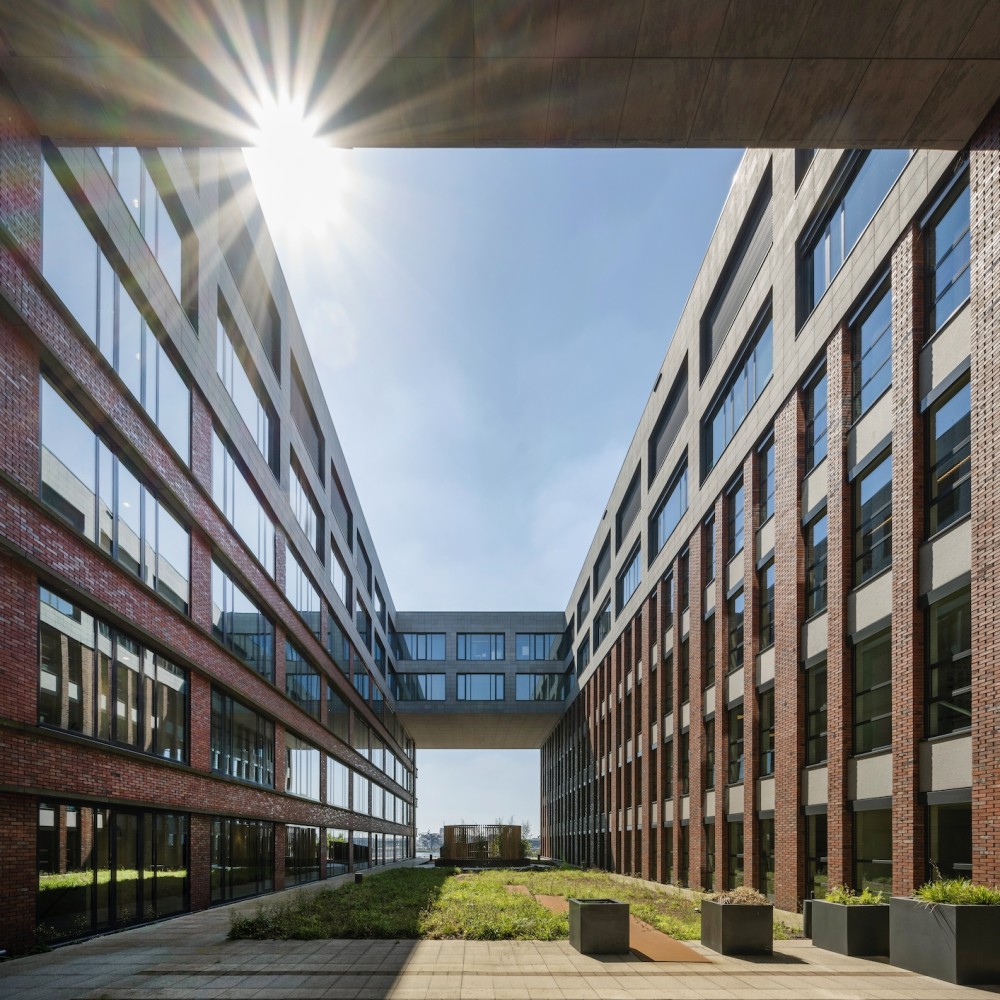 Binnenplaats van een modern kantoorcomplex met bakstenen gevels en glazen ramen, met de zon stralend bovenin.