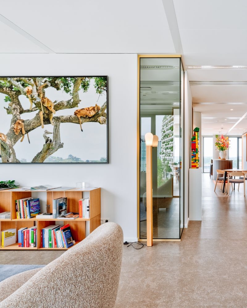 Medewerker zit aan een vergadertafel met laptops en kijkt aandachtig op tijdens een overleg. Op de achtergrond hangen schetsen en notities op een glazen wand, wat een creatieve en samenwerkende werkomgeving laat zien.
