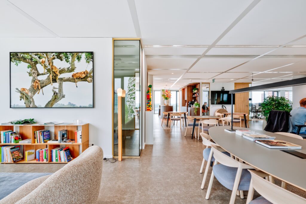 Moderne kantoorruimte met gedeelde werkplekken, lange tafel, boekenkast en zithoek in een lichte en open werkomgeving.