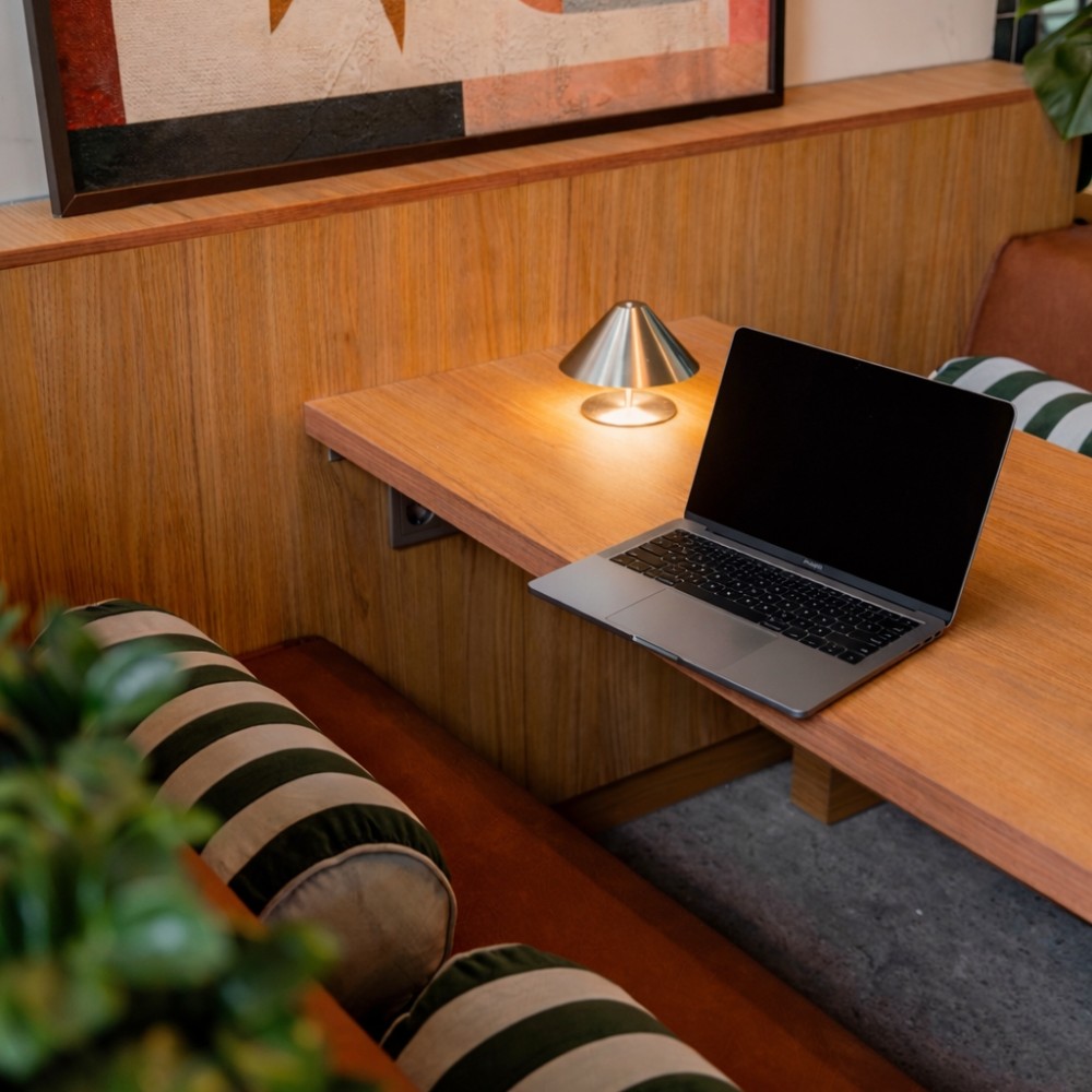 Een moderne werkomgeving met een laptop op een houten tafel en een kleine lamp ernaast in een kantoorruimte.