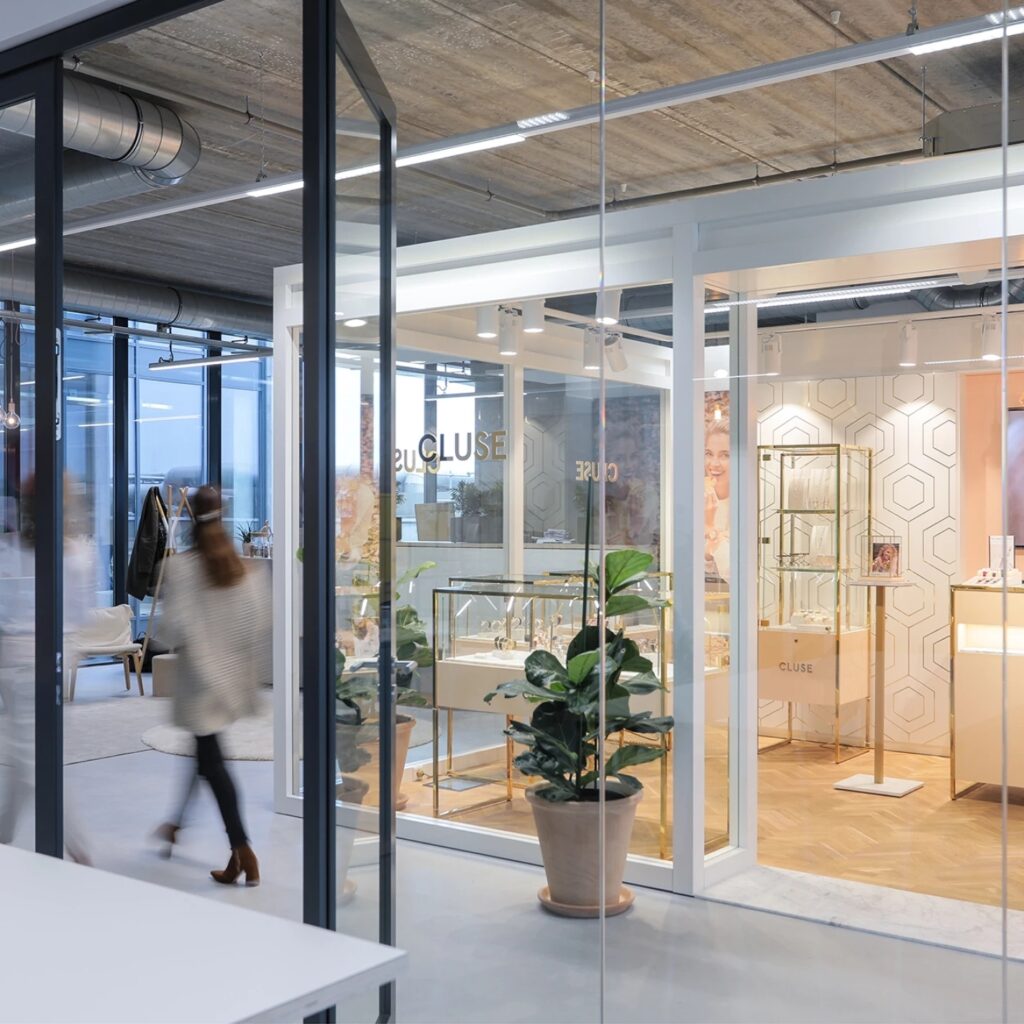 Moderne kantoorruimte met glazen wanden, planten en showroomachtige inrichting.