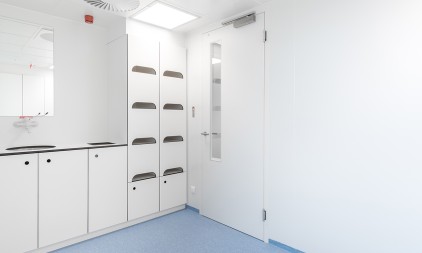 Een witte, steriele laboratoriumruimte met kasten en een deur.