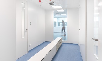 Een moderne, witte gang met blauwe vloerbedekking en een persoon die door het raam zichtbaar is.